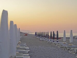 Una spiaggia con file di lettini e ombrelloni.