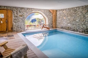 A stone-walled indoor pool with a wooden deck and a view of the outdoors. - Chalet - Saint André (Saint-André)