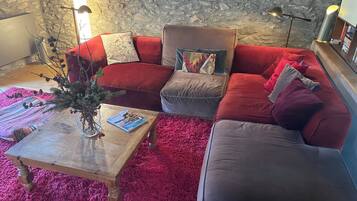 A cozy living room with a stone wall, a red and grey sectional sofa, a wooden coffee table, and a red shag rug.