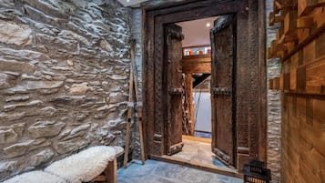 A rustic interior with a stone wall, wooden door, bench, and a candle on the floor.