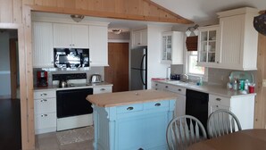 Una cucina con mobili bianchi, soffitto in legno, isola centrale e tavolo da pranzo con sedie.