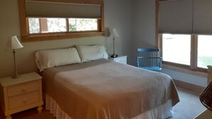 Una camera da letto con un letto, due comodini, una lampada, una sedia e una finestra con persiane.