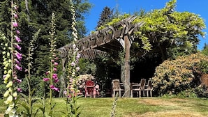 Un jardin agrémenté d’une pergola en bois, d’un espace détente et de plantes à fleurs hautes.