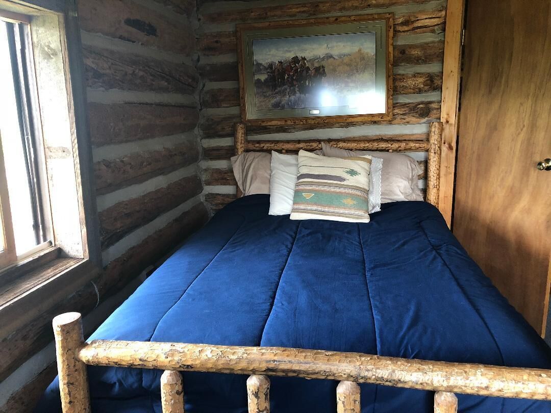 A log cabin room with a bed, wooden headboard, and a painting on the wall.