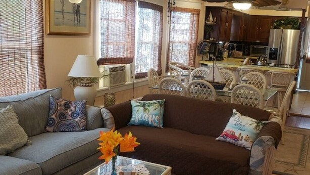 Uma sala de estar com sofá, mesa de centro com um vaso de flores e área de jantar com cadeiras e mesa.