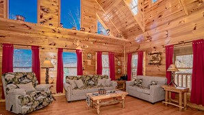 A log cabin interior with two sofas, a coffee table, and red curtains. - 🏔️ American Dream: Log Cabin with Sauna, Hot Tub, and Firepit🌲 (Sevierville)
