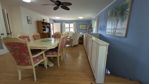 Un comedor con mesa de madera, sillas con estampado floral y un ventilador de techo.
