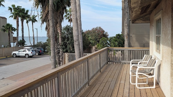 Une terrasse en bois, agrémentée de chaises, donnant sur une rue où sont garées des voitures et où l’on peut admirer des palmiers.