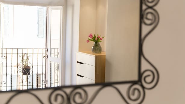 A balcony with a wrought iron railing, a hanging light fixture, and a small table with a vase of flowers.