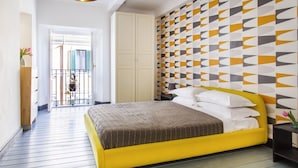 A bedroom with a yellow bed, a geometric patterned wall, and a balcony with a view.