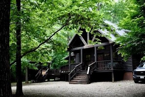 A log cabin with a porch, stairs, and a vehicle parked nearby. - Deep in the hardwoods near the end of Timber Creek Trail, you will discover this (Broken Bow)