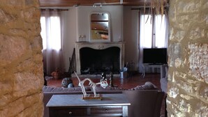 A rustic living room with exposed wooden beams, a stone wall, a fireplace, a television, and a patterned rug.