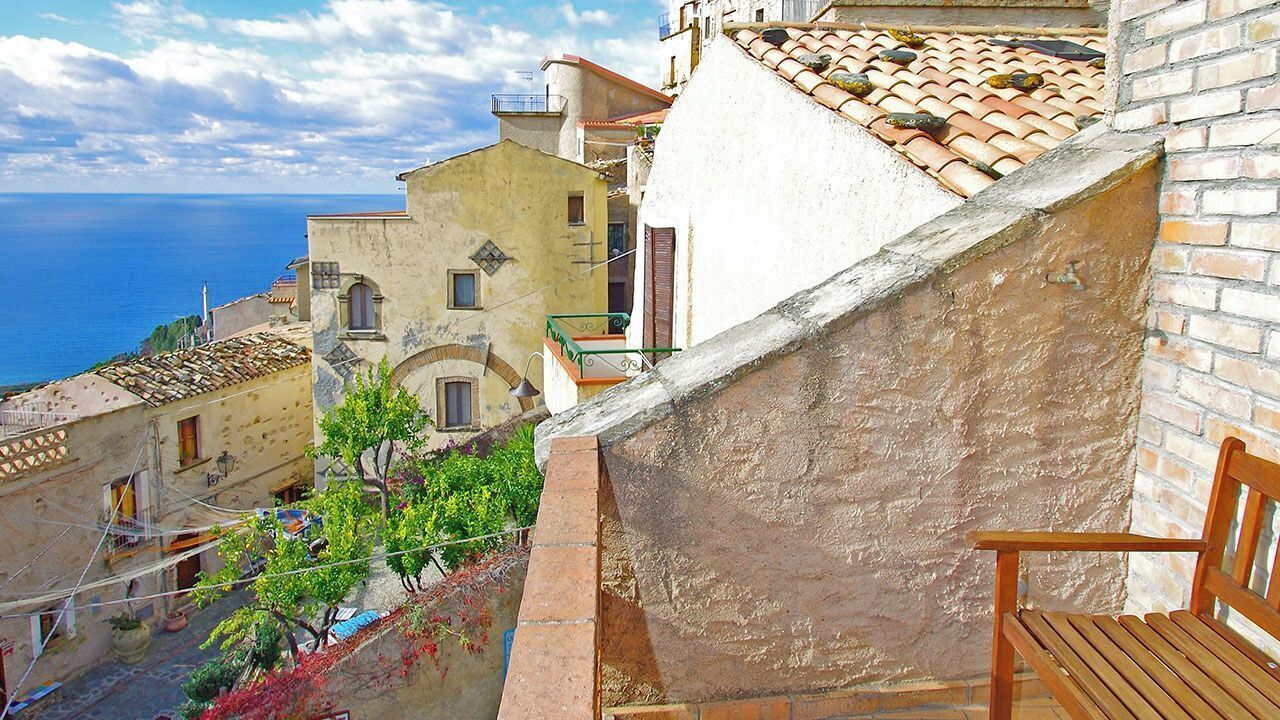 A narrow street with buildings on both sides, a wooden bench, and a view of the sea.
