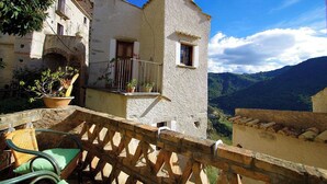 Un edifici rústic amb un balcó, plantes en testos i una cadira de vimet.