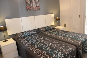 Une chambre à coucher avec un grand lit, deux tables de chevet, une commode, une lampe fixée au mur et une porte.