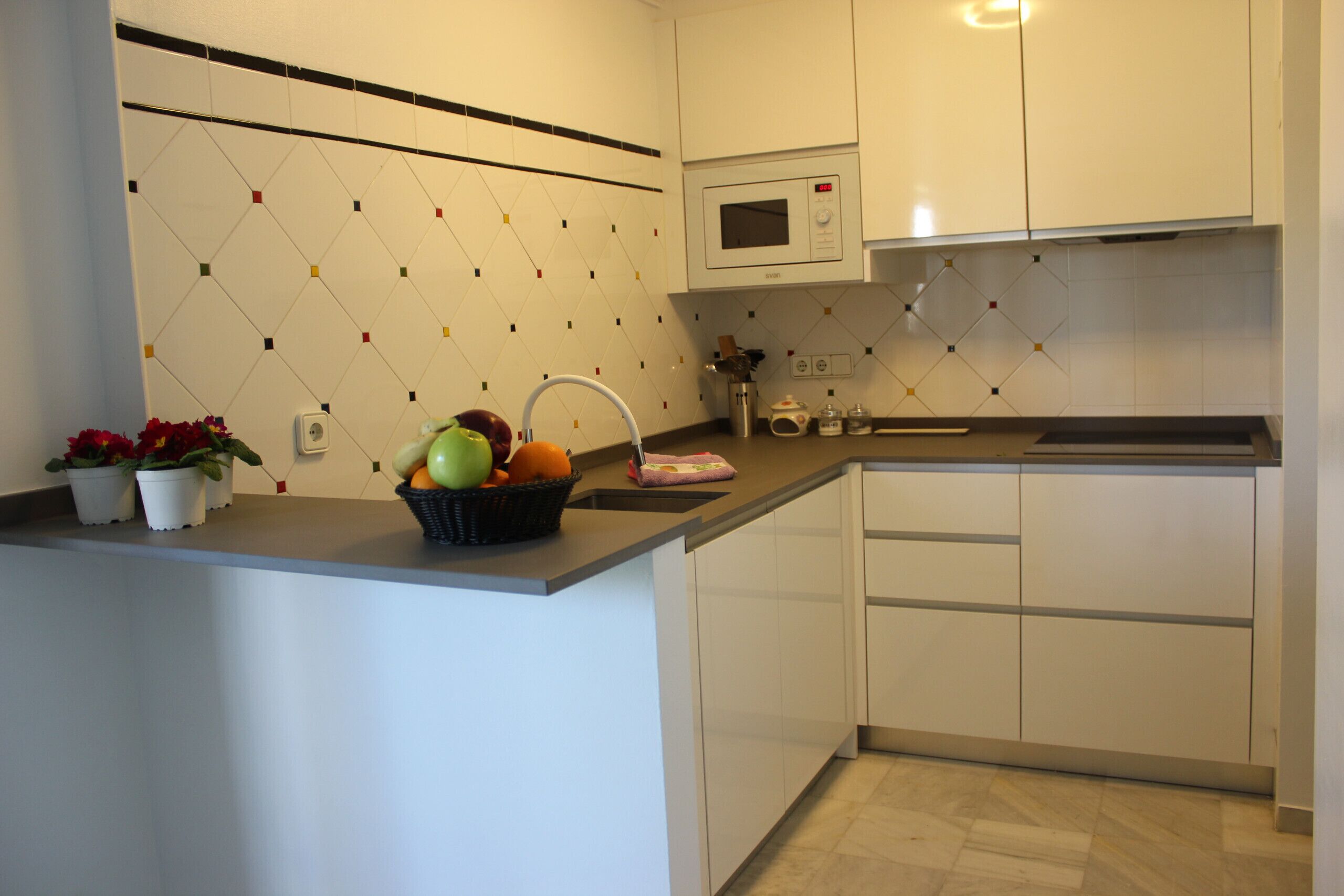 A modern kitchen with white cabinets, a microwave, and a fruit bowl on the counter.