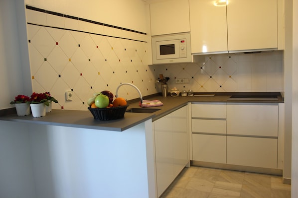 Cozinha moderna com armários brancos, micro-ondas e uma tigela de frutas na bancada.