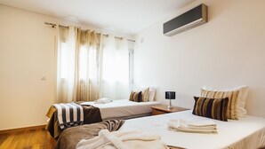 Hotelkamer met twee bedden, een nachtkastje met lamp, een raam met gordijnen en een airconditioning.