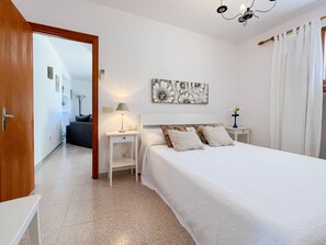 Quarto com cama, mesa de cabeceira, abajur, quadro na parede e porta para outro cômodo.