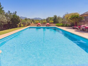 Piscina retangular com água azul cristalina, ladeada por um deck de concreto. Há espreguiçadeiras com almofadas vermelhas na borda da piscina.