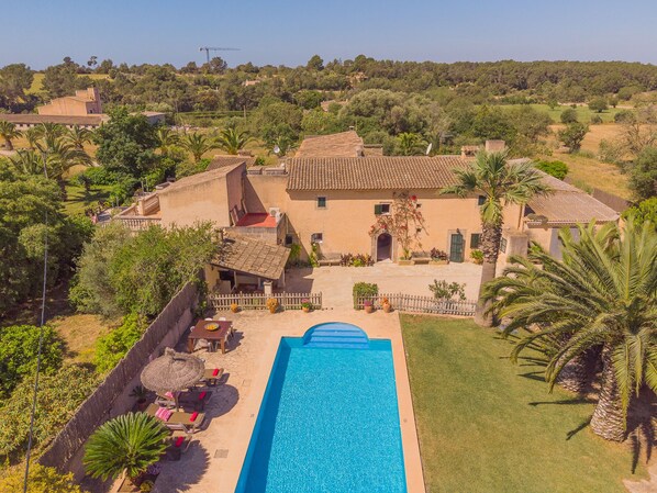 Une grande maison avec une piscine, entourée de palmiers et située dans un paysage vallonné.