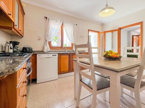 Uma cozinha com armários de madeira, lava-louças, pia e uma mesa de jantar com cadeiras.