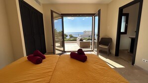 A room with a bed, two red towels, a wicker chair, and a view of the sea through a glass door. - Luxury villa with panoramic sea views for 12 people, large pool, BBQ house  (Cala Murada)