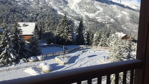 A snow-covered mountain landscape with a ski resort, including a building with a sloped roof and a fenced area with snow-covered trees. - High-end apartment, immediate access to ski slopes (Les Allues)