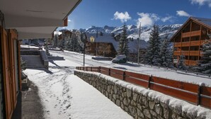 A snow-covered street with a stone wall and wooden buildings, including a chalet with a balcony. - High-end apartment, immediate access to ski slopes (Les Allues)
