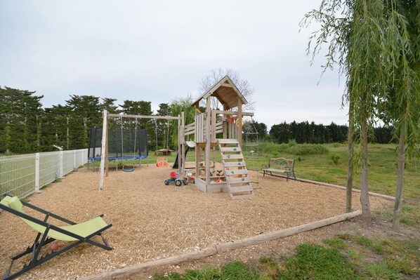 Een speeltuin met een houten klimstructuur, schommels en een glijbaan.