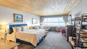 Ein gemütliches Zimmer mit einem Bett, einem Schreibtisch, einem Sessel, einem Bücherregal und einem großen Fenster mit Meerblick.