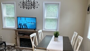 A dining area with a wooden table, white chairs, a TV displaying a welcome message, and a decorative welcome sign on the wall. - LEEDS A GREAT ESCAPE (Leeds)