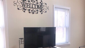 A living room with a flat-screen TV on a wooden entertainment center, a 'WELCOME' sign above, and a patterned rug on the floor. - LEEDS A GREAT ESCAPE (Leeds)