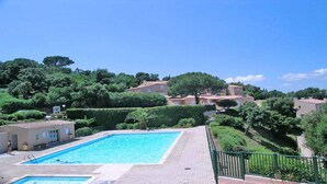 A swimming pool with a tiled deck, surrounded by greenery and buildings with red-tiled roofs.