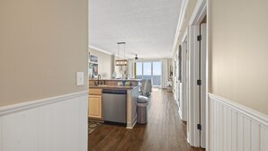 A kitchen with a dishwasher, a sink, and a dining area with a chair and table. - Emerald Isle 1607 - Front row beach chair service included! Affordable rates! (Panama City Beach)