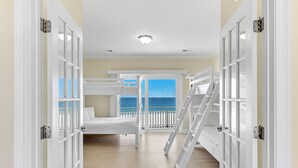 A room with bunk beds, a balcony with a view of the sea, and a staircase.