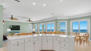 A spacious kitchen with a large island, wooden chairs, and a view of the ocean.