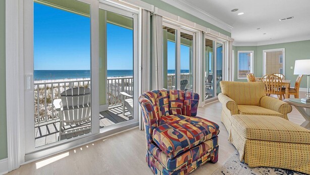 A spacious room with large windows overlooking the beach, a colorful armchair, a yellow sofa, and a dining area with wooden chairs.