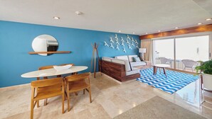 Ein modernes Hotelzimmer mit Essbereich, einer Sofagruppe, einem großen Spiegel und Blick ins Freie.