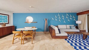 Ein modernes Wohnzimmer mit blauer Akzentwand, einem runden Spiegel, einem Holzesstisch mit Stühlen, einer Couch mit Kissen und einem gemusterten Teppich.