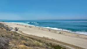 A beach with a concrete walkway, a lifeguard tower, and a clear blue sky. - Sand (1 bedroom / 1 bath) (Carlsbad)