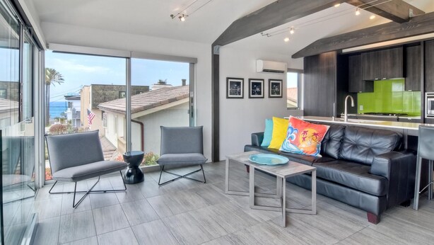 A modern living room with a black leather sofa, two grey armchairs, and a coffee table. A large window offers a view of the cityscape. - Sand (1 bedroom / 1 bath) (Carlsbad)