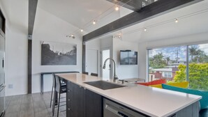 A modern kitchen with a large island, dark cabinetry, and a view of the outside. - Sand (1 bedroom / 1 bath) (Carlsbad)