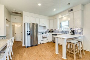 Enjoy cooking in this well-equipped kitchen with a central island, bar stools, stainless steel appliances, and white cabinetry.