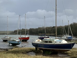 A row of boats moored along a calm waterway, with grassy banks and trees in the background. - Family-friendly cottage - walk to stunning beach (Angle)