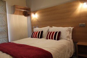 A hotel room with a wooden headboard, a bed with white bedding and striped pillows, a red throw blanket, and a nightstand.