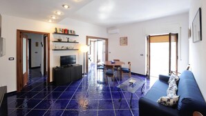 A spacious living area with a blue-tiled floor, a television, a dining table with chairs, and a sofa. - MAIORI "Reginella" house with terraces & sea view (MAIORI)