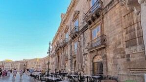 Un bâtiment historique doté de balcons richement décorés et d’un espace café avec des places assises en plein air.
