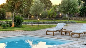 Una piscina con sillas de descanso y un jardín bien cuidado.
