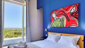 Una habitación de hotel con cama, un ventanal grande y un cuadro en la pared.